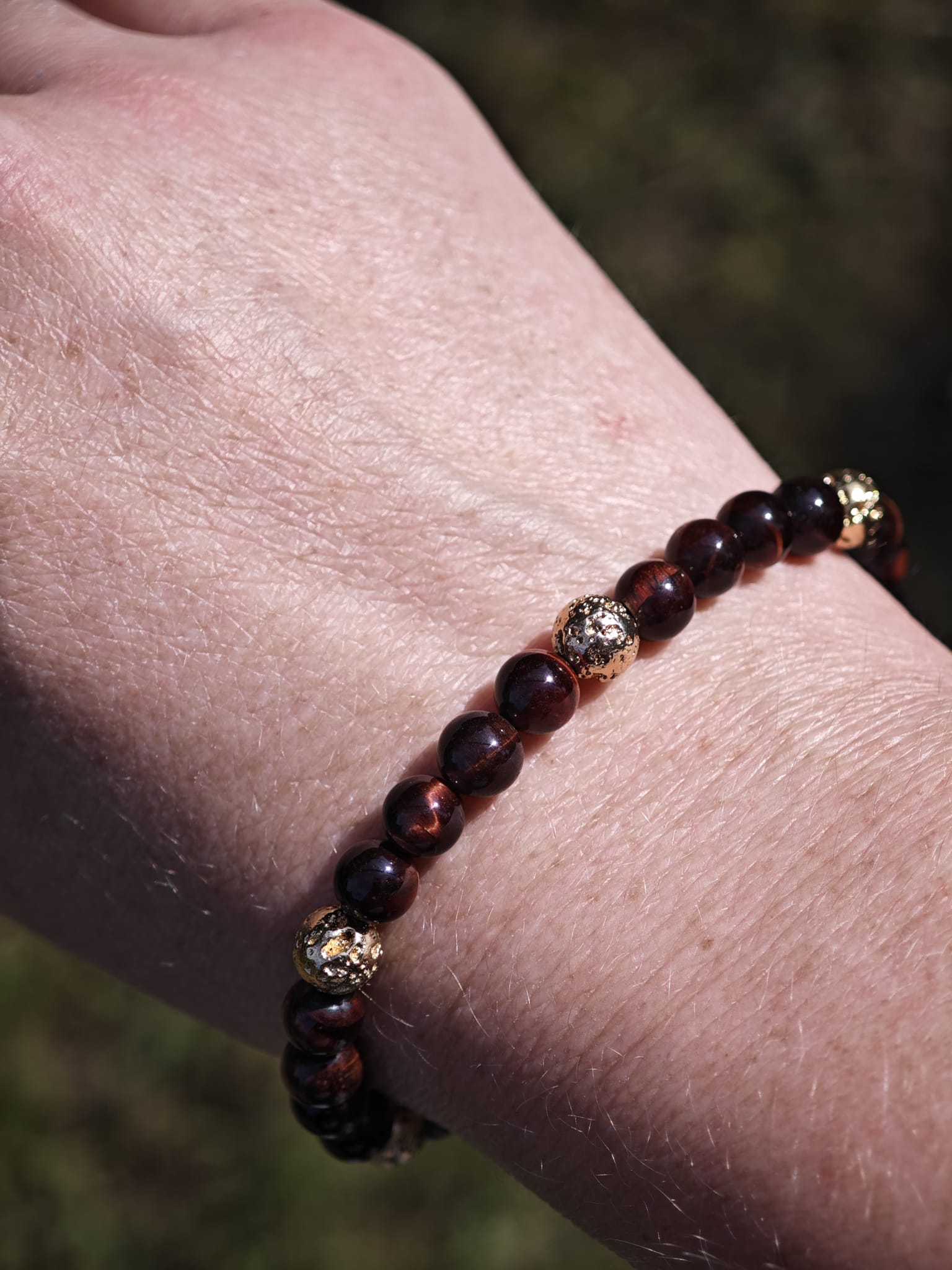 Dunkelrot-braunes Perlenarmband an einem Handgelenk im Freien.